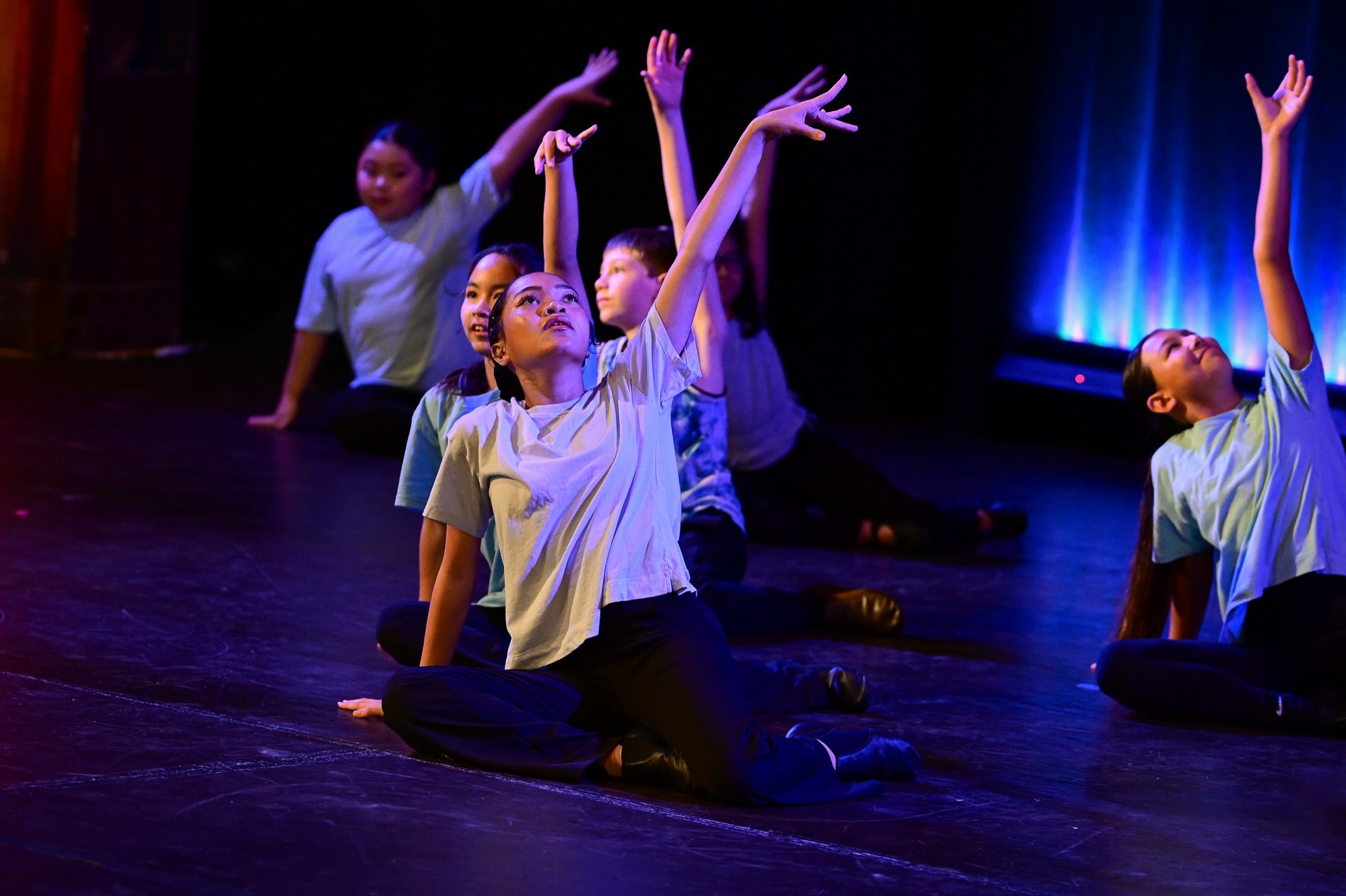Young dancers with arms raised reaching upward on stage